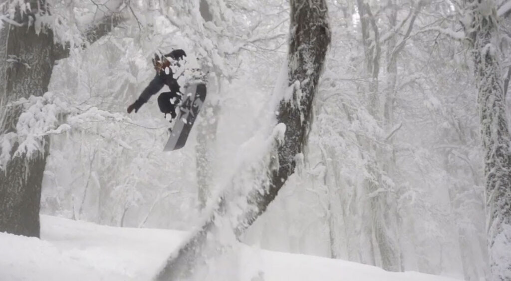 Jones pro snowboarder powder run through the trees in Cerro Lopez